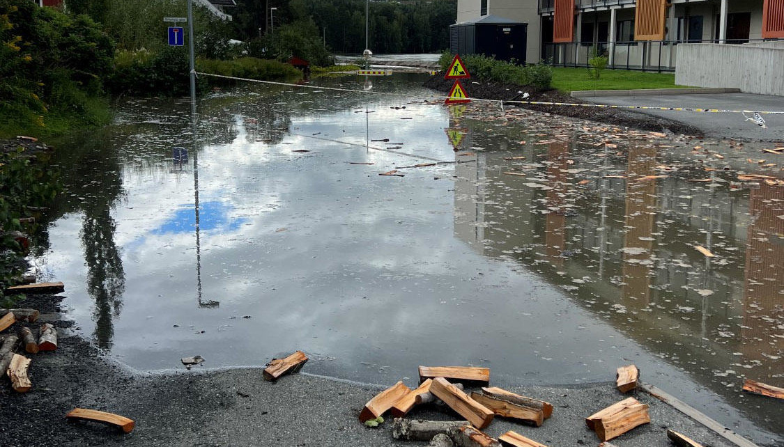 Flom, vann på avsperret vei med hus rundt.